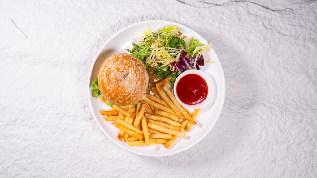 Appetizing burger with crispy fries and fresh salad served on a white plate.